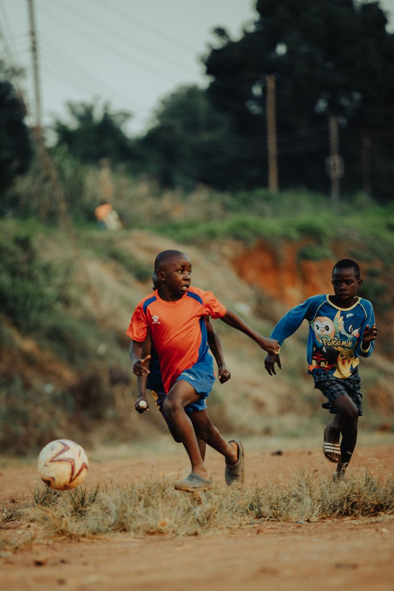 Two boys playing football with the ball visible on a field in Kampala, Uganda